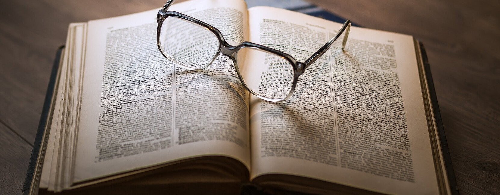Symbolbild eines geöffneten Buches mit einer Brille darauf