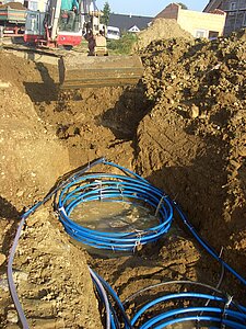 Geothermie-Baugrube mit spiralförmigen Rohrkollektoren, schlammigem Wasser und Bagger im Einsatz.